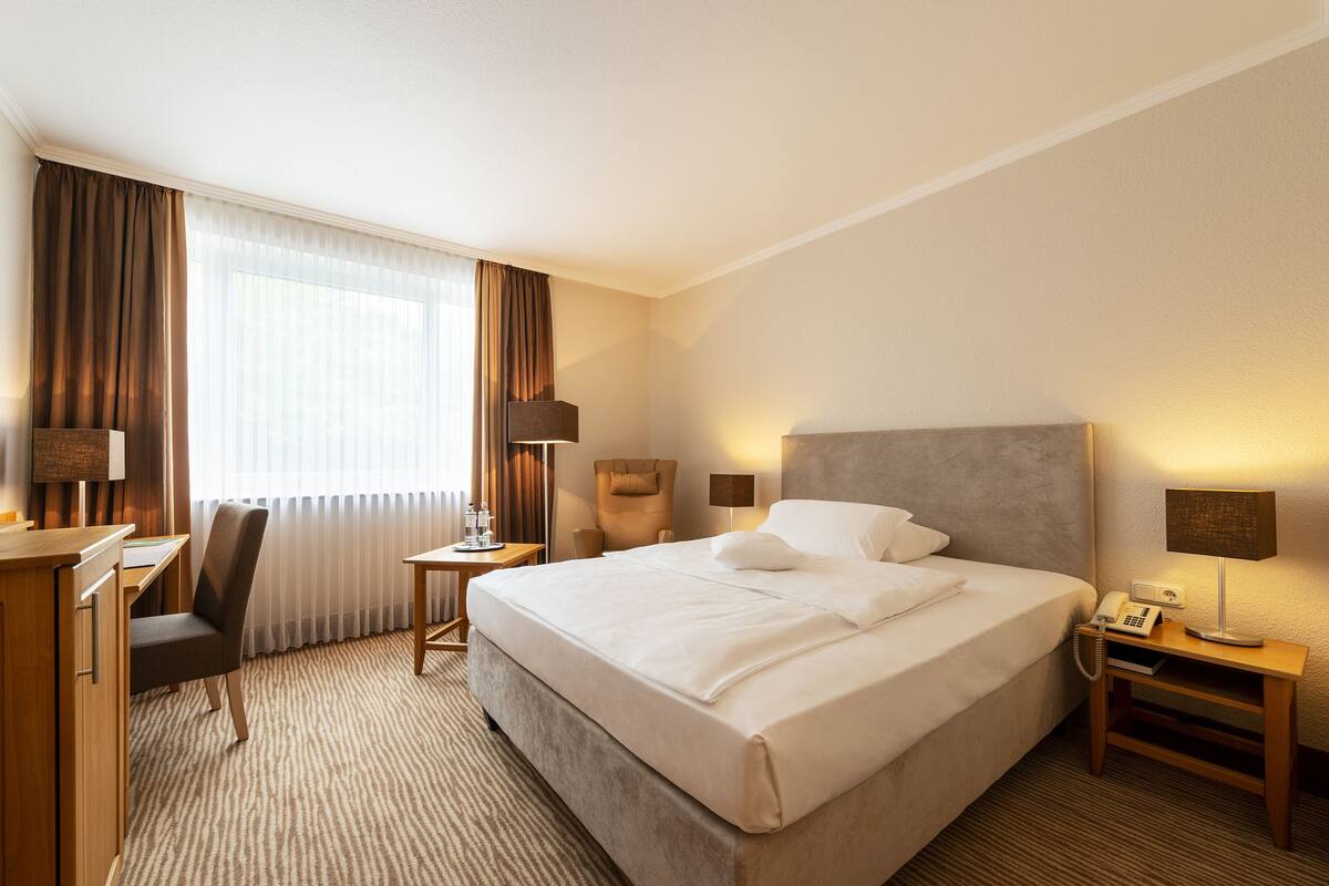 Een hotelkamer met een groot bed, een bureau, een stoel, een lamp en een telefoon.