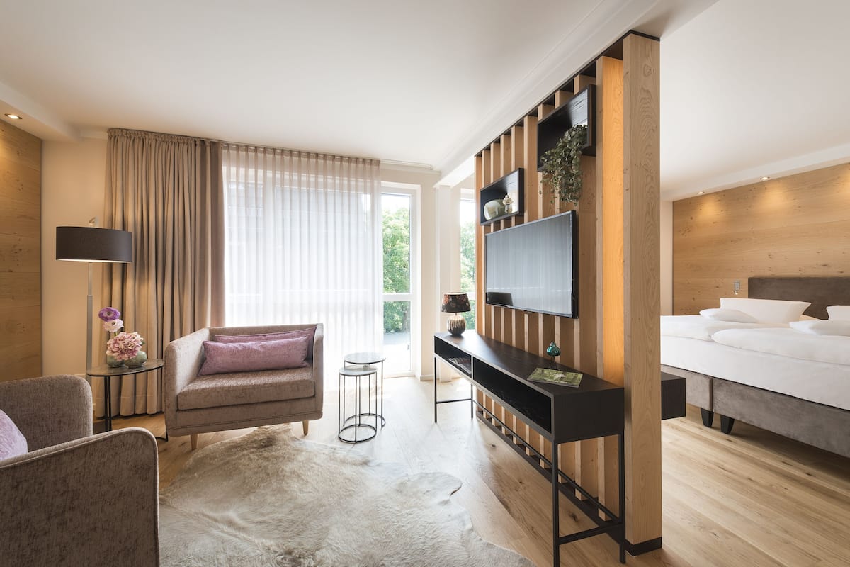 Een moderne hotelkamer met een bed, een bank, een aan de muur bevestigde televisie en een kleine bijzettafel met een lamp.