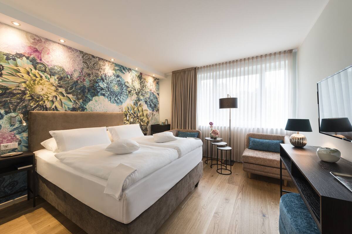 Een moderne hotelkamer met een groot bed, een bureau, een stoel en een decoratieve muurschildering.