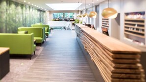 Een modern interieur met groene zitplaatsen, een houten receptiebalie en uitzicht op de omgeving.