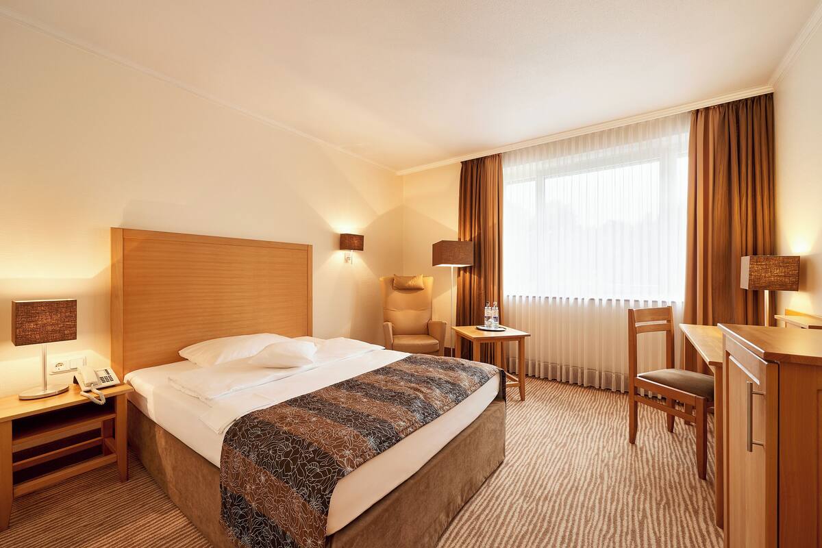 Een hotelkamer met een groot bed, een bureau met een lamp, een stoel en een kleine tafel met een fles.
