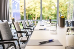 A conference room with a long table, chairs, and a glass of water.