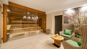 Een modern interieur met een sauna met glazen wanden, een houten trap, een rieten stoel met kussen en een kleine ronde tafel.