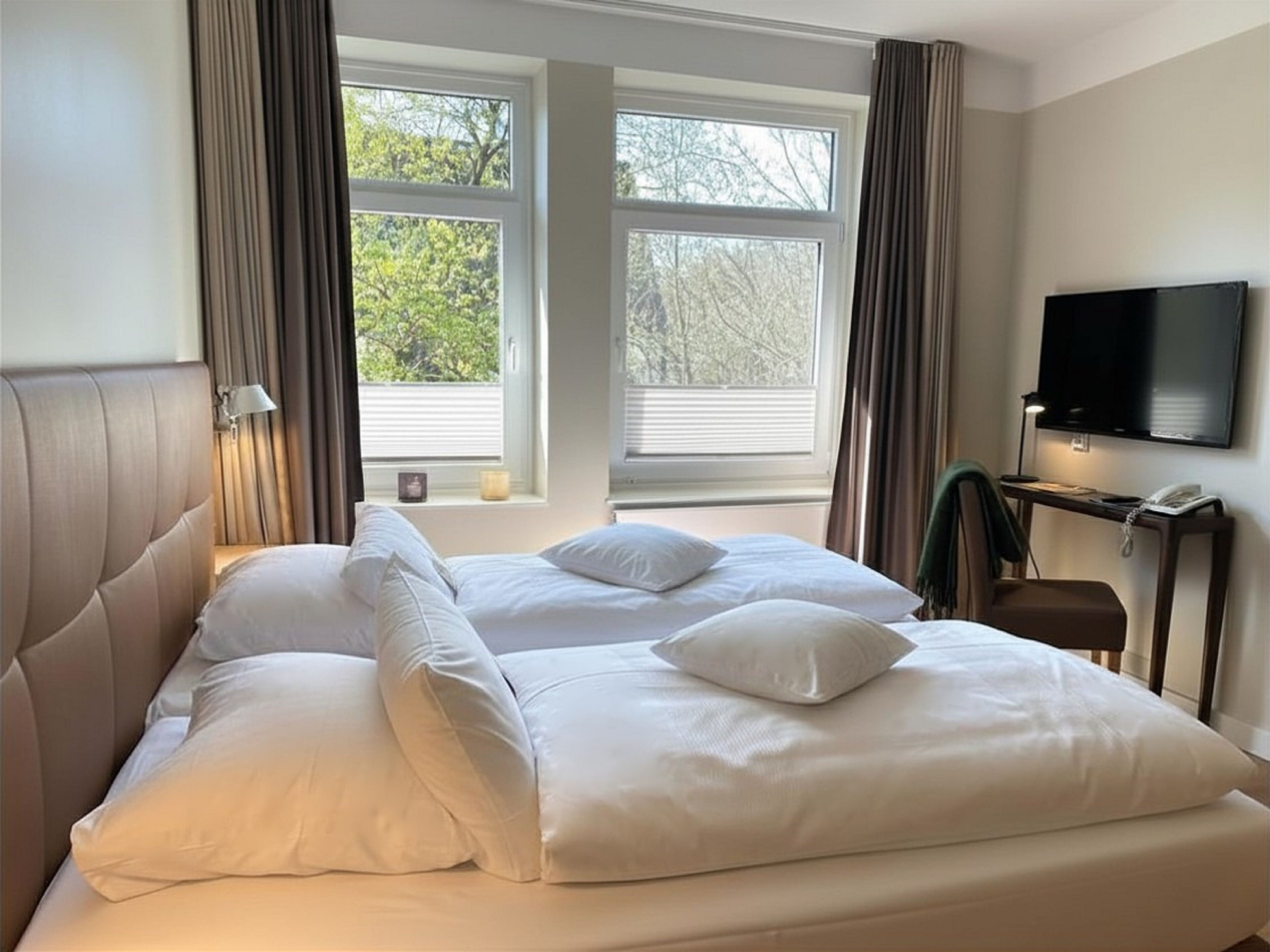 Habitación de hotel con una cama grande, televisión de pantalla plana y dos ventanas con cortinas.