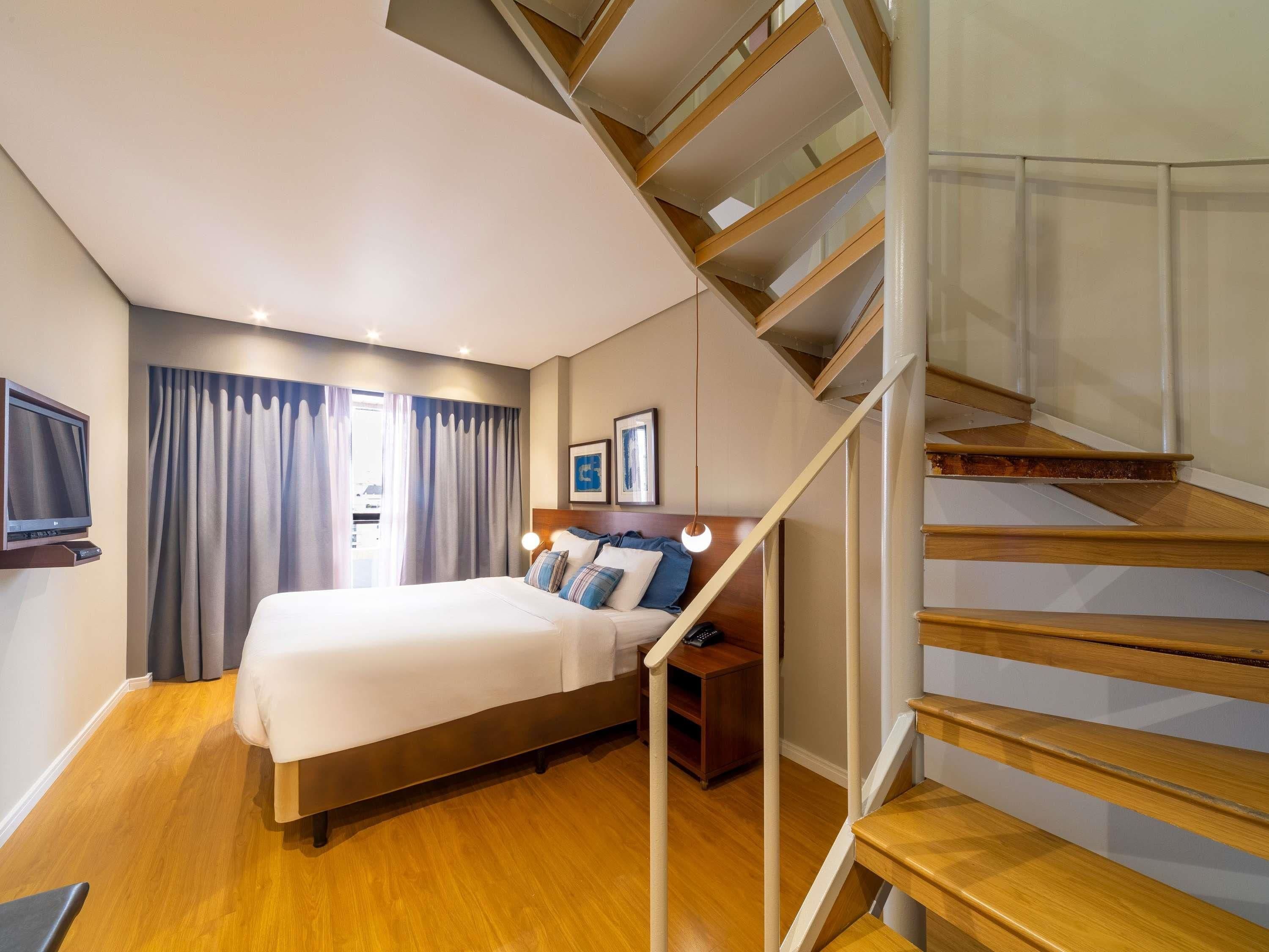 Una habitación de hotel con cama, televisor, escritorio y escalera.