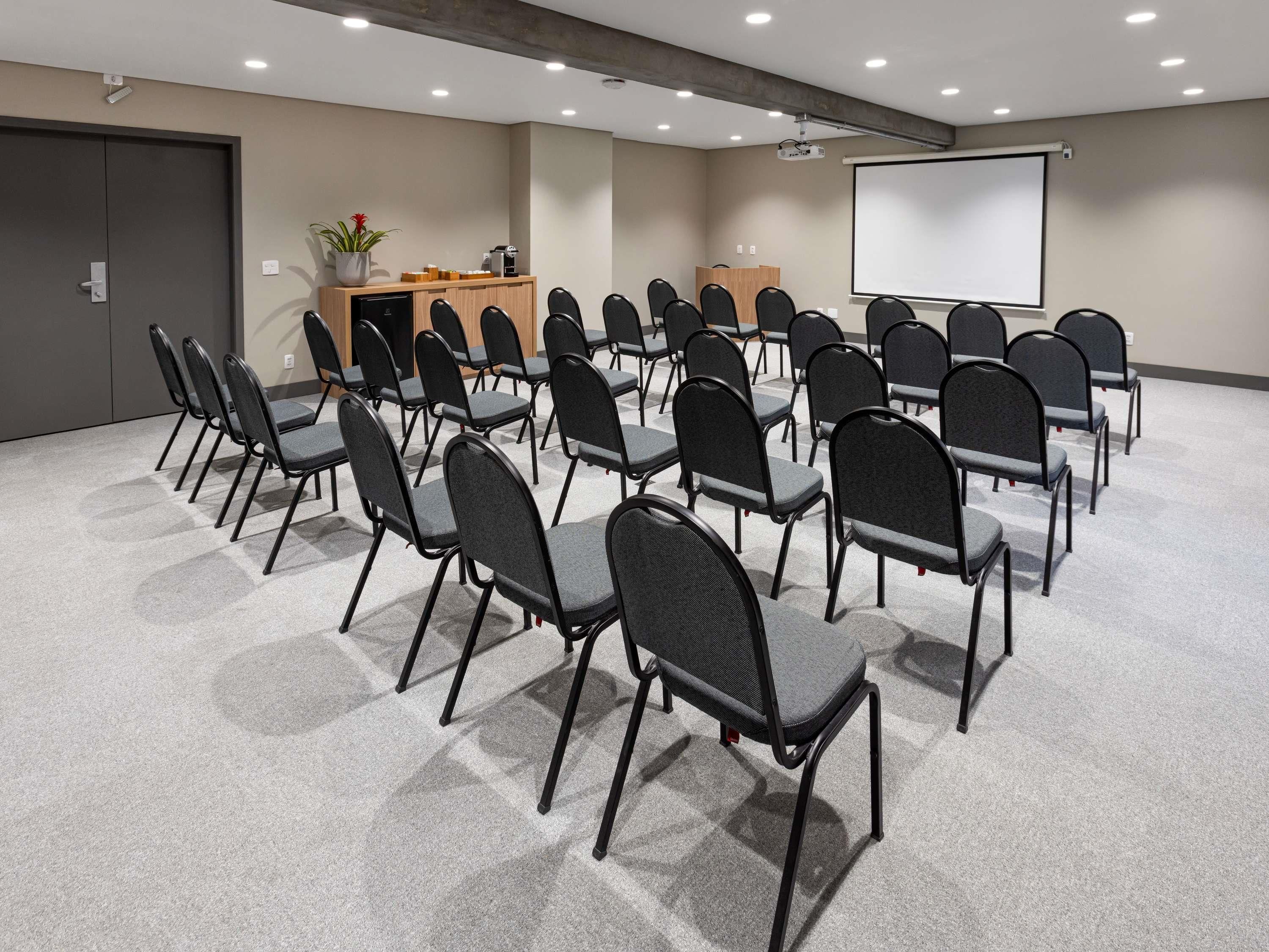A conference room with rows of chairs, a projector screen, and a coffee station.