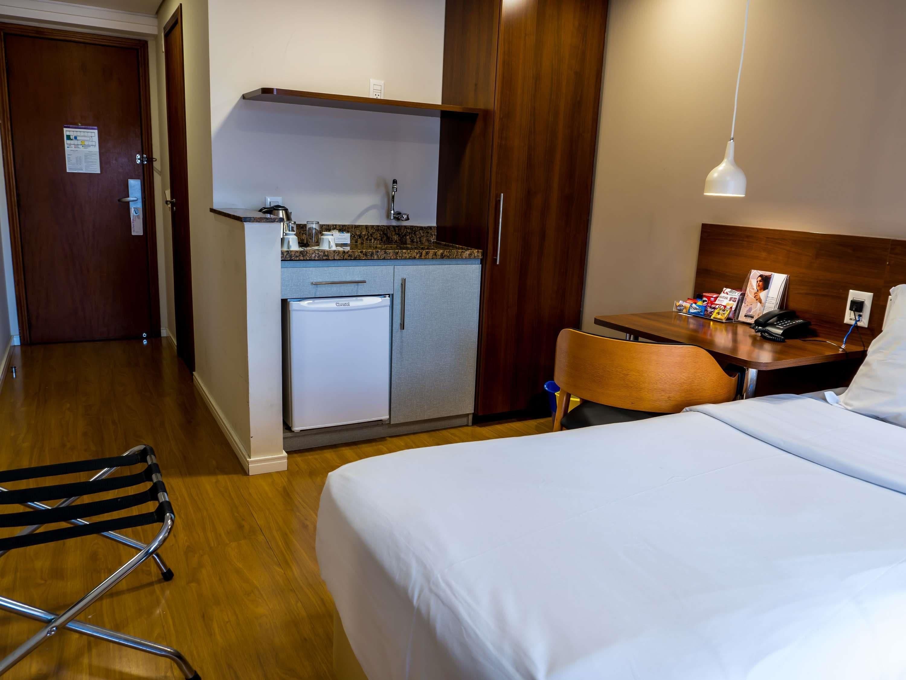 Una habitación de hotel con una cama, un escritorio con una silla, una kitchenette y piso de madera.