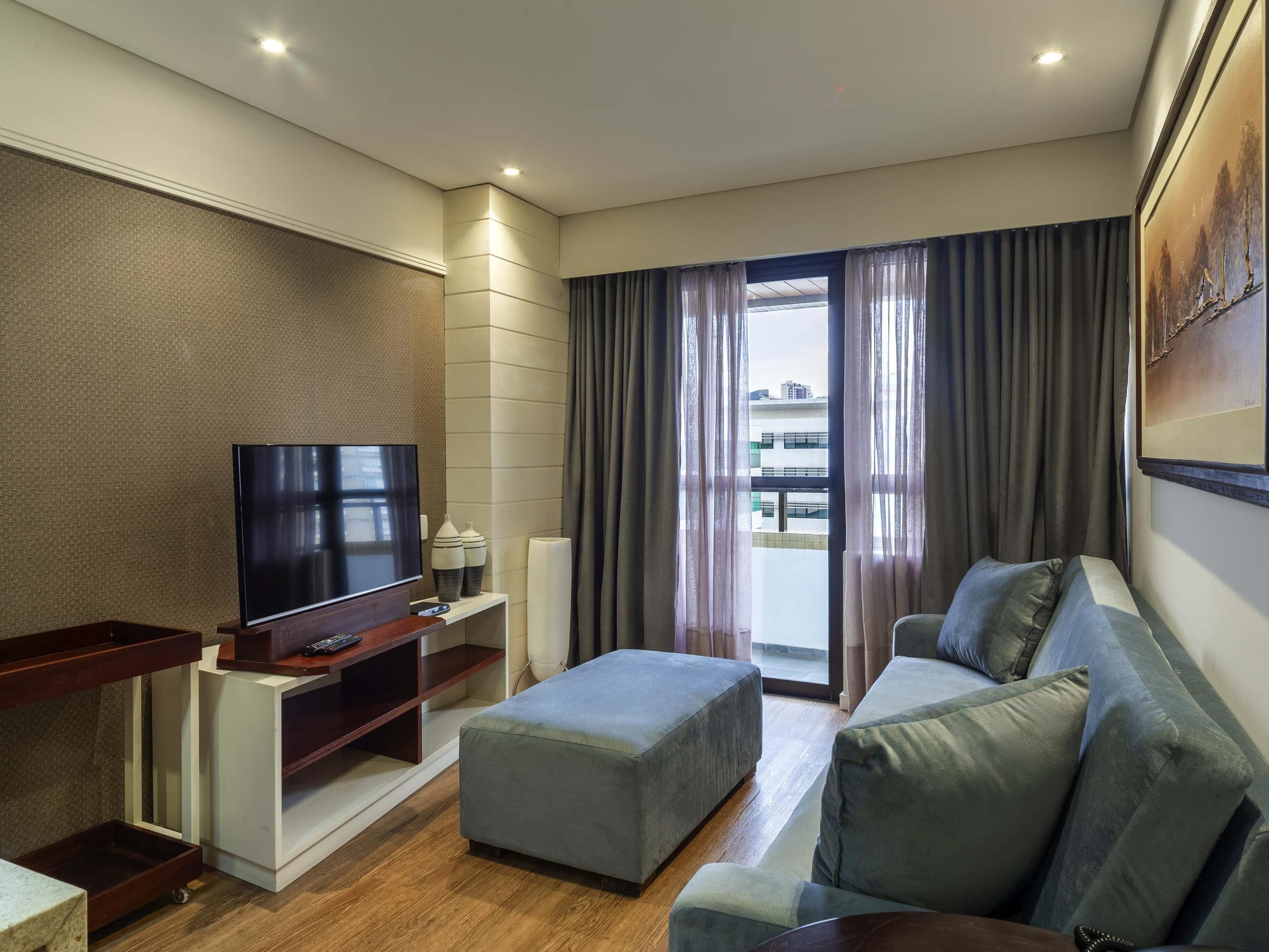 Uma sala de estar moderna com televisão de tela plana, sofá, mesa de centro e varanda com cortinas.