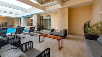 Uma área de piscina interior moderna, com espreguiçadeiras, uma mesa de madeira e plantas em vasos.