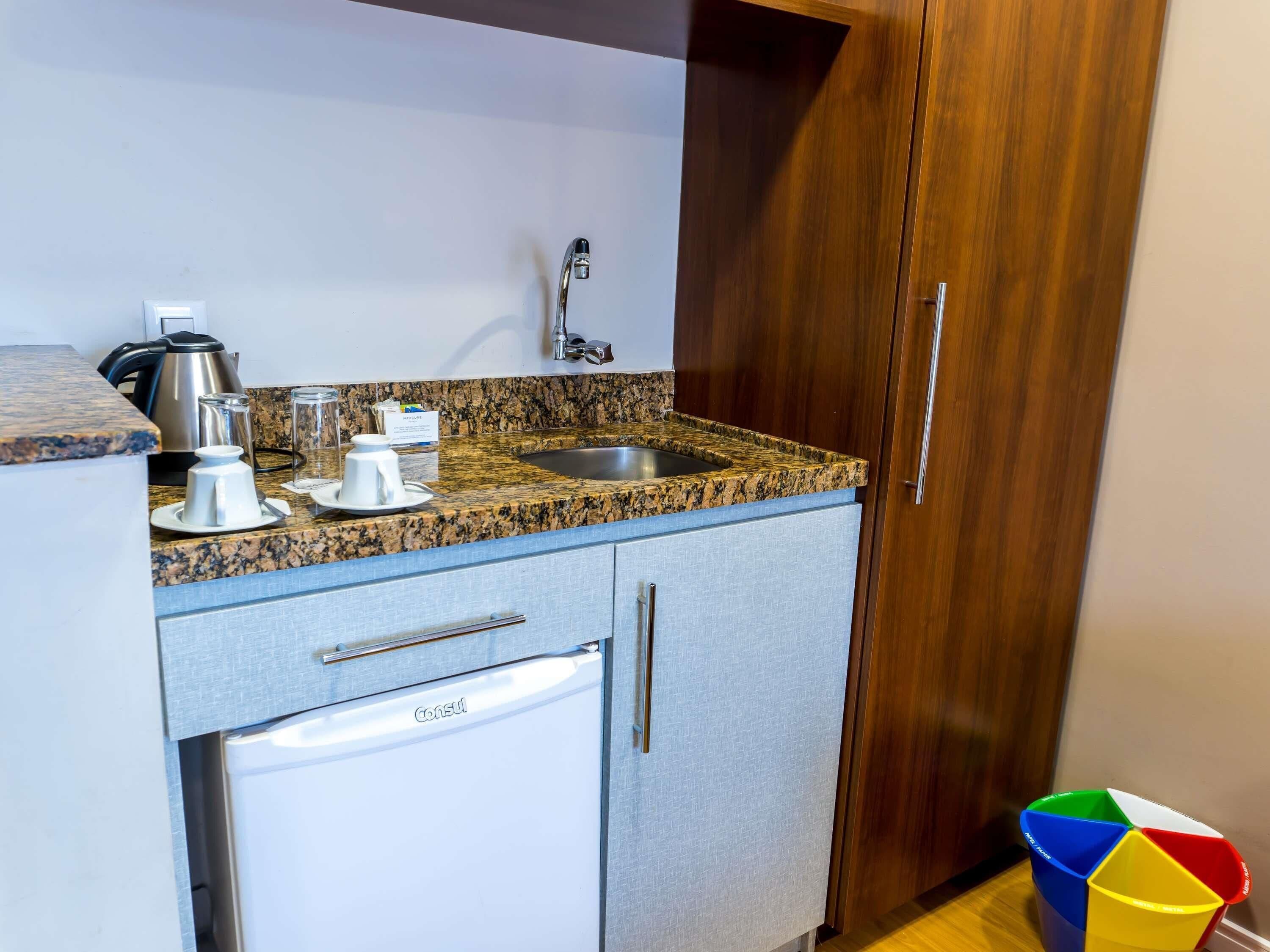 A kitchen with granite countertops, a stainless steel sink, a coffee maker, a kettle, and a dishwasher.