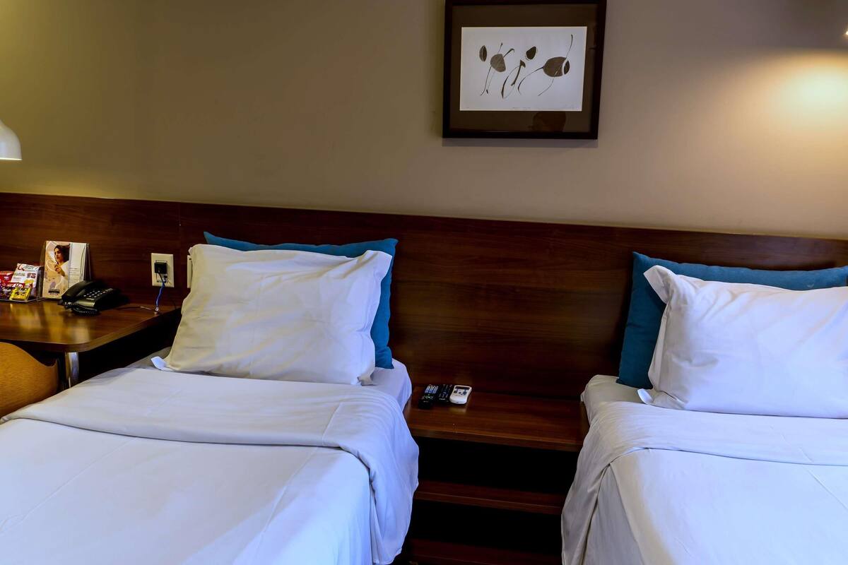 Habitación de hotel con dos camas, una mesita de noche, una obra de arte enmarcada en la pared y un teléfono sobre la mesita de noche.