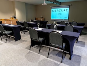 Une salle de conférence équipée de tables, de chaises et d’un écran de projection affichant le texte « MERCURE HOTEL CURITIBA GOLDEN PASS ».