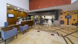 Zona de recepción de hotel con un mostrador de madera, asientos, una pantalla digital y una decoración interior moderna.