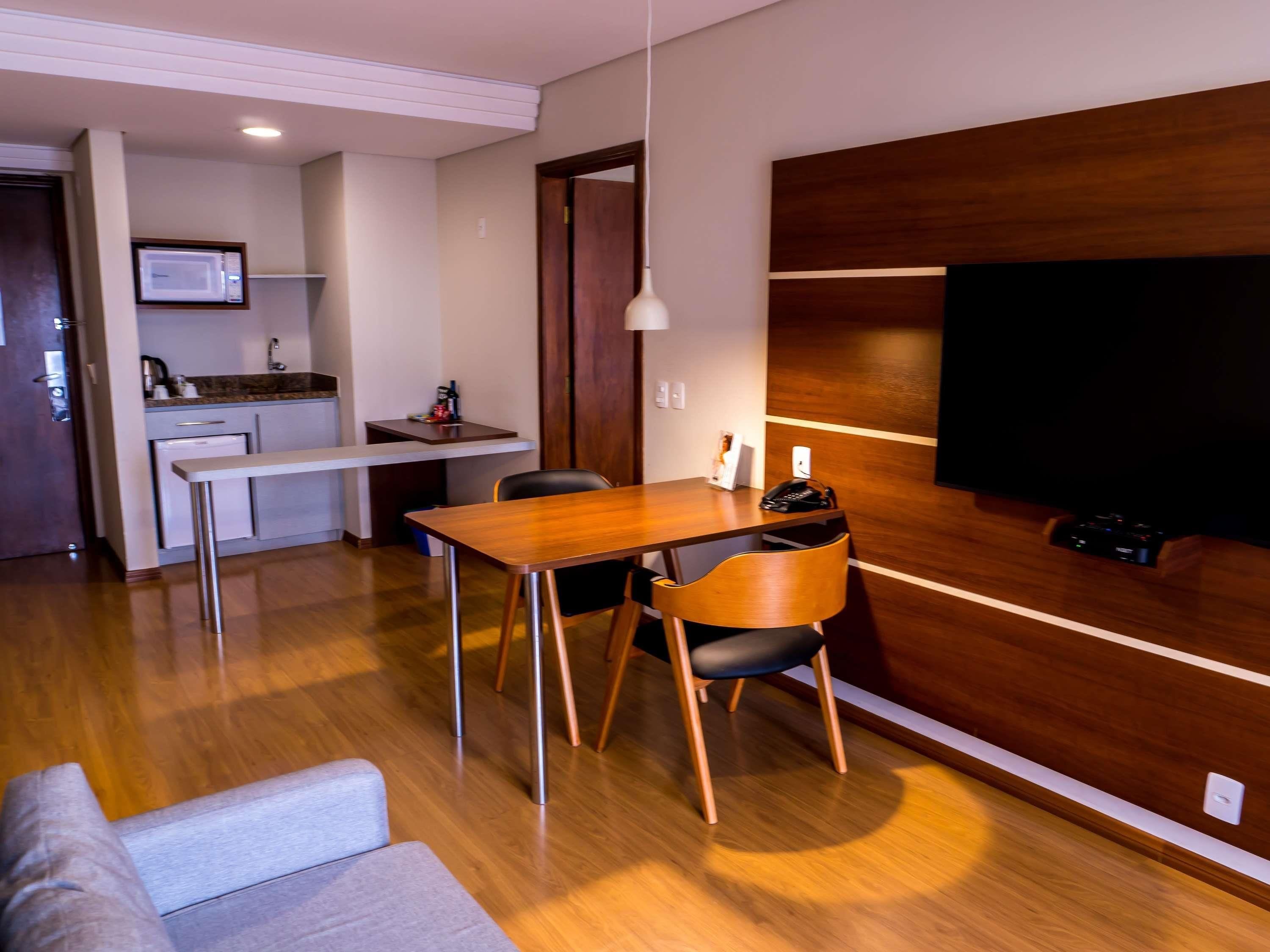 A modern living room with a wooden dining table, a sofa, and a TV mounted on a wooden wall.