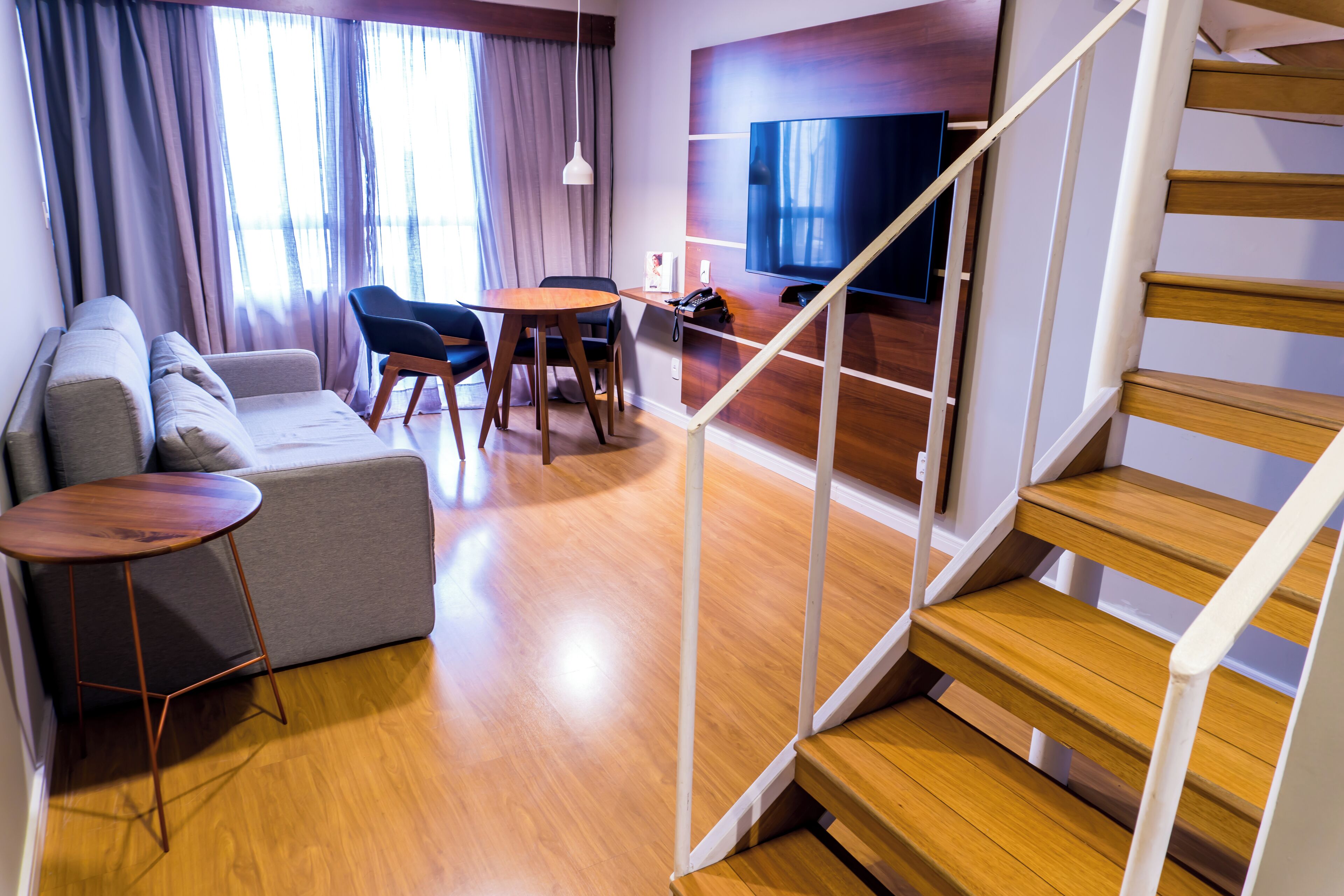 A modern living room with a sofa, chairs, a small table, a TV, and a wooden staircase.