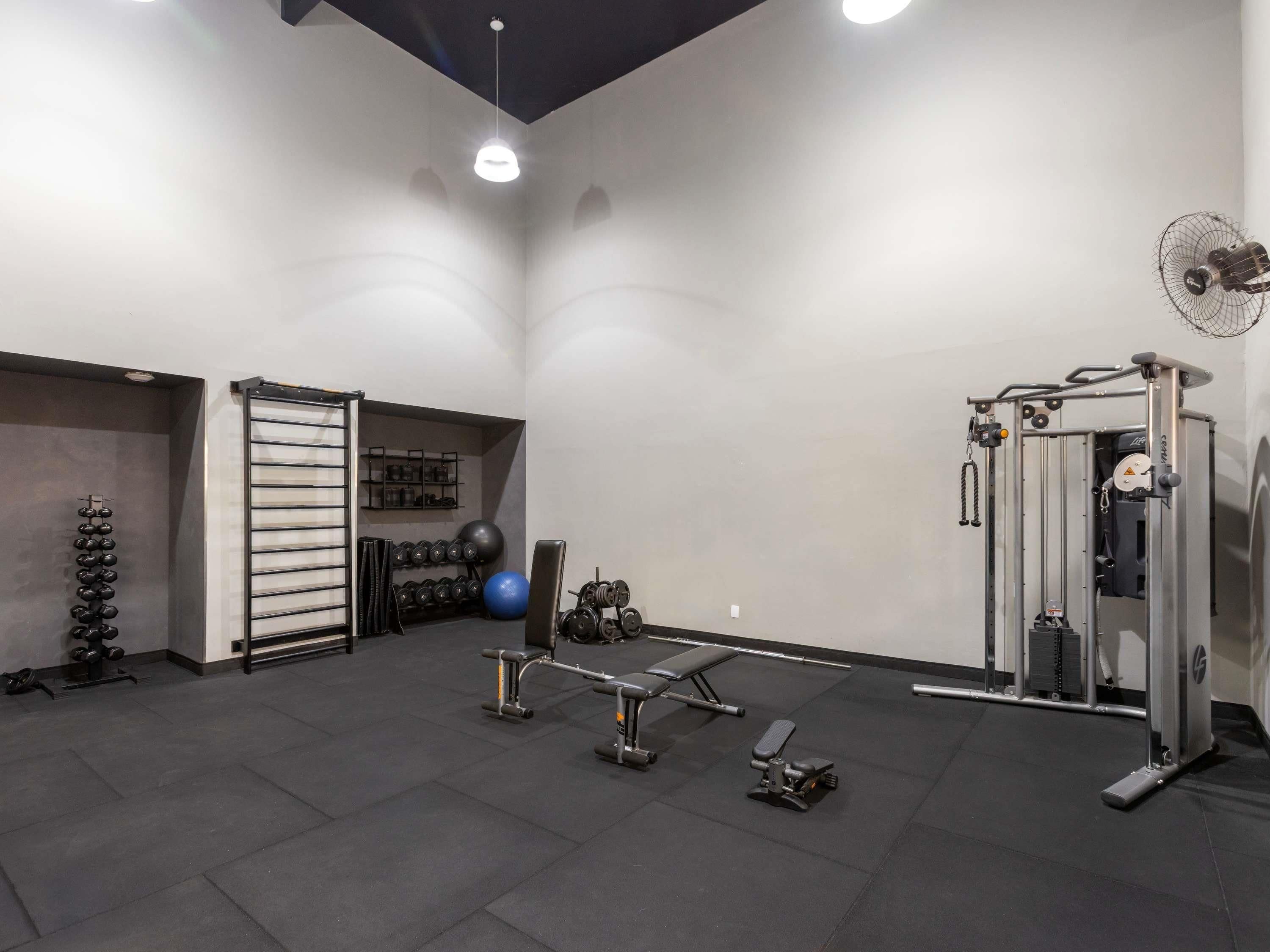A gym with weight racks, dumbbells, a bench press, and a cable machine.