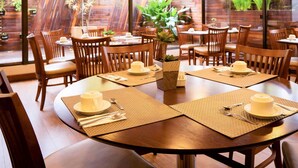 Comedor con mesas redondas, sillas de madera y plantas en macetas.