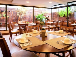 A dining area with round tables, wooden chairs, and potted plants. - Mercure Curitiba Golden Hotel (Curitiba)
