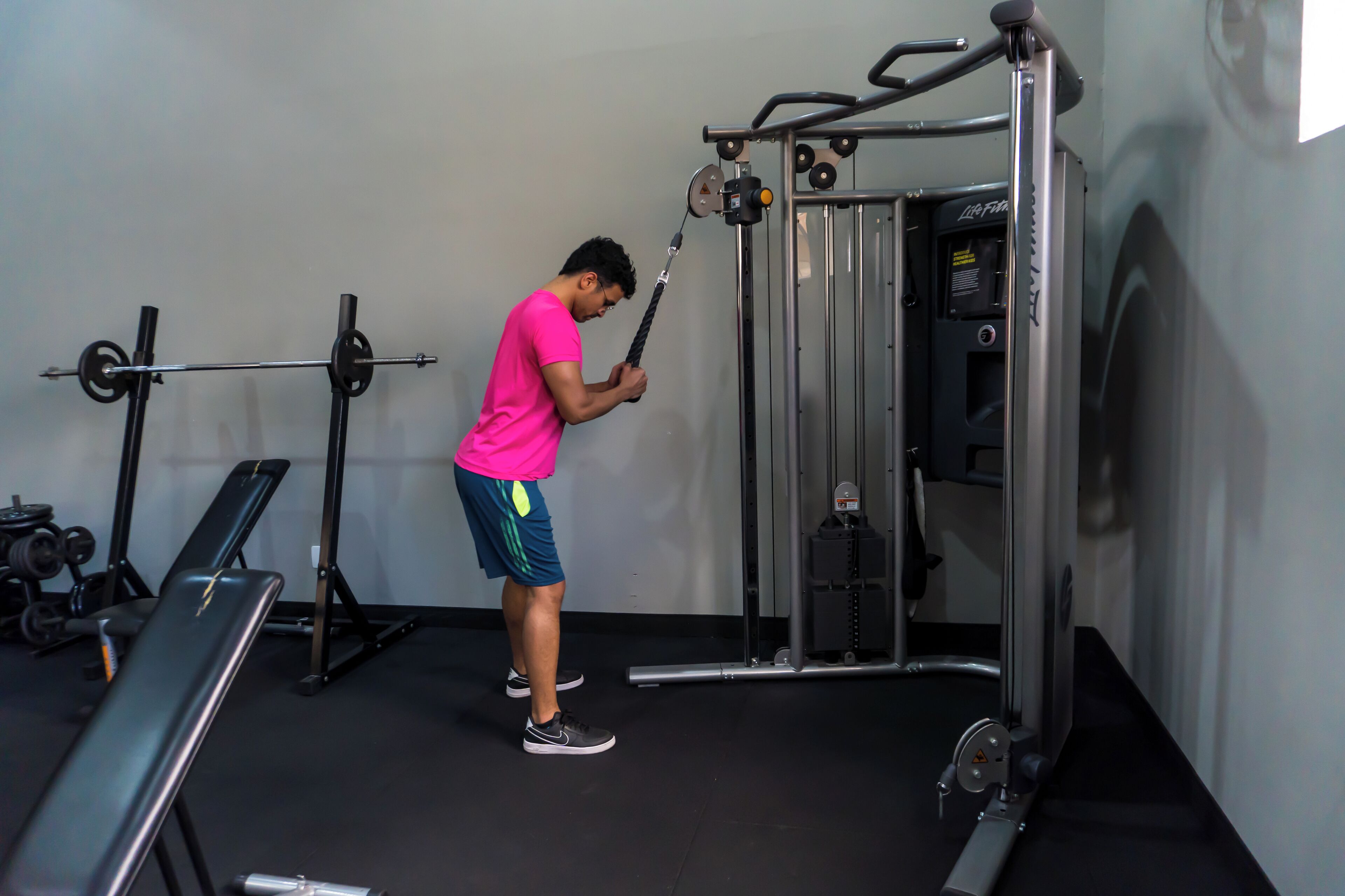 Un gimnasio con equipo de levantamiento de pesas, una banca y un televisor montado en la pared.