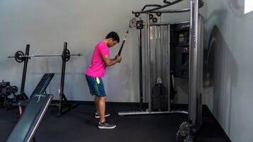 Un gimnasio con equipo de levantamiento de pesas, una banca y un televisor montado en la pared.