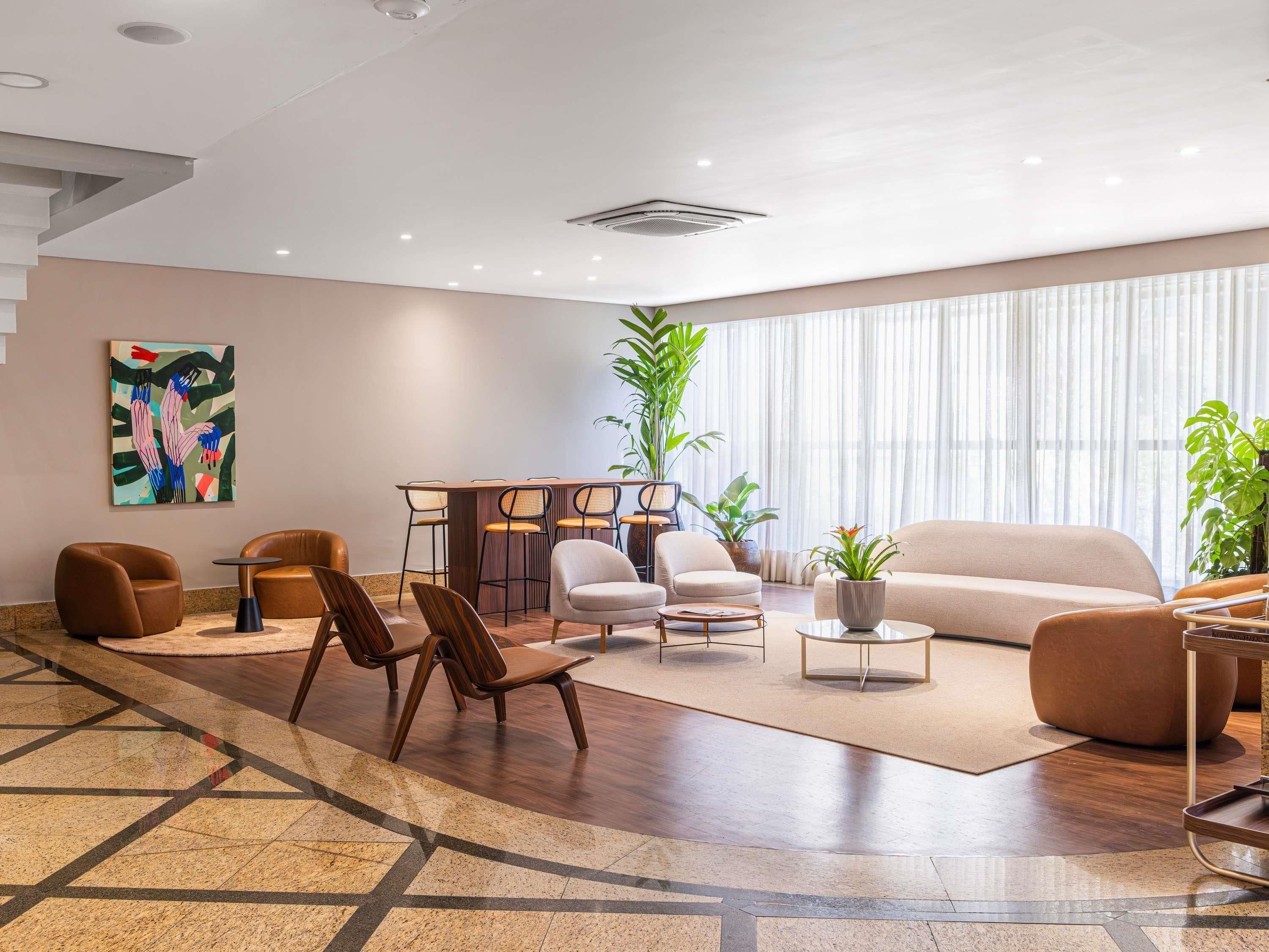 Un vestíbulo de hotel moderno con zona de estar, un bar y un amplio ventanal con cortinas.