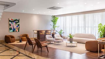 Un vestíbulo de hotel moderno con zona de estar, un bar y un amplio ventanal con cortinas.