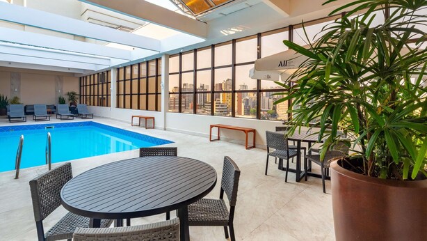 Una piscina interior con sillones de descanso y una mesa, rodeada de amplias ventanas y una planta en maceta.