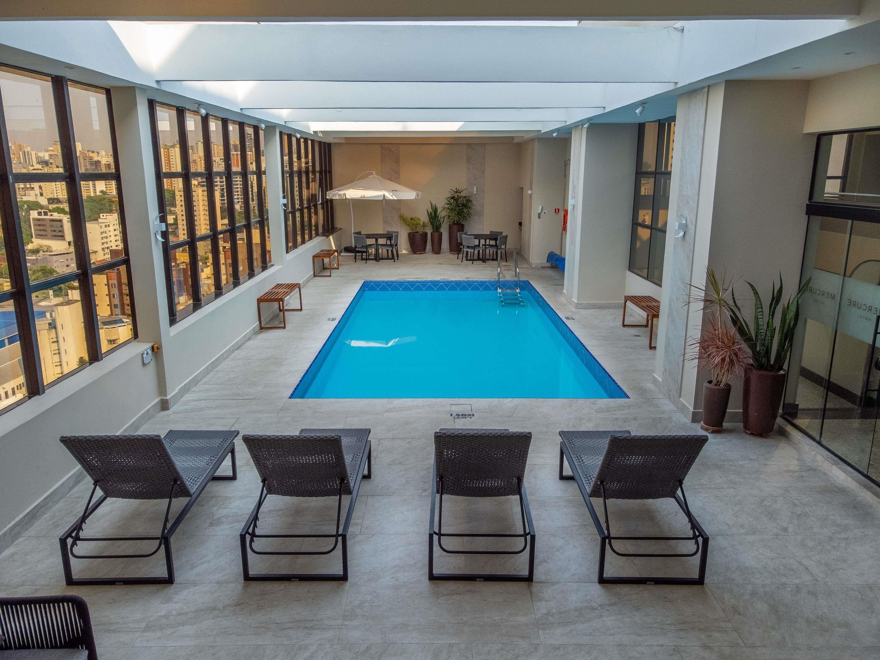 A rooftop pool with lounge chairs, a table, and potted plants.