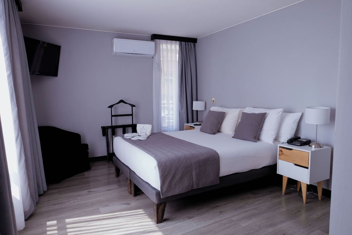 A modern hotel room with a large bed, bedside tables, a TV, and a wardrobe.