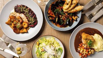 A table set with multiple dishes including steak, mussels, and a salad, with cutlery and a glass of wine.