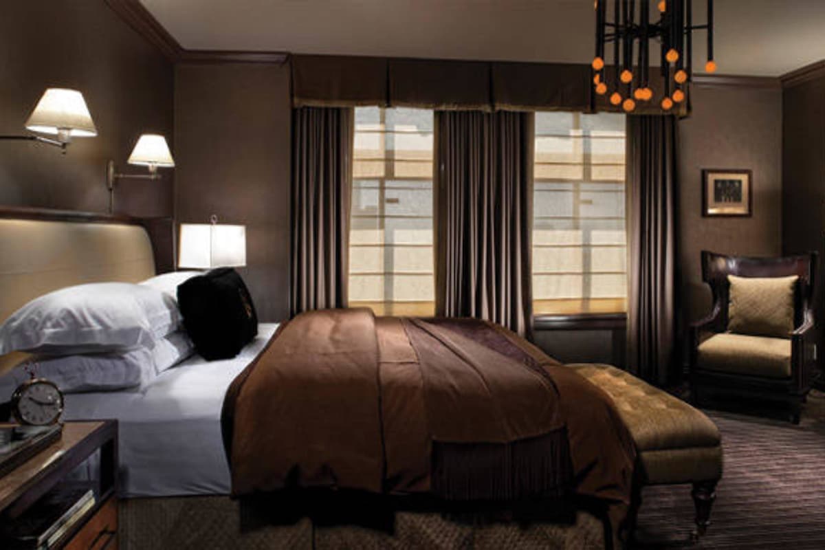 Une chambre d’hôtel avec un grand lit, une chaise, un bureau avec une lampe et une fenêtre avec des rideaux.