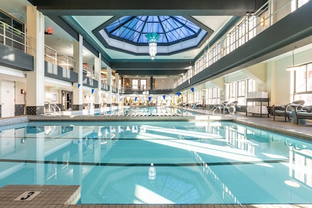 A large indoor swimming pool with a skylight ceiling, multiple levels with balconies, and a seating area with chairs and tables.