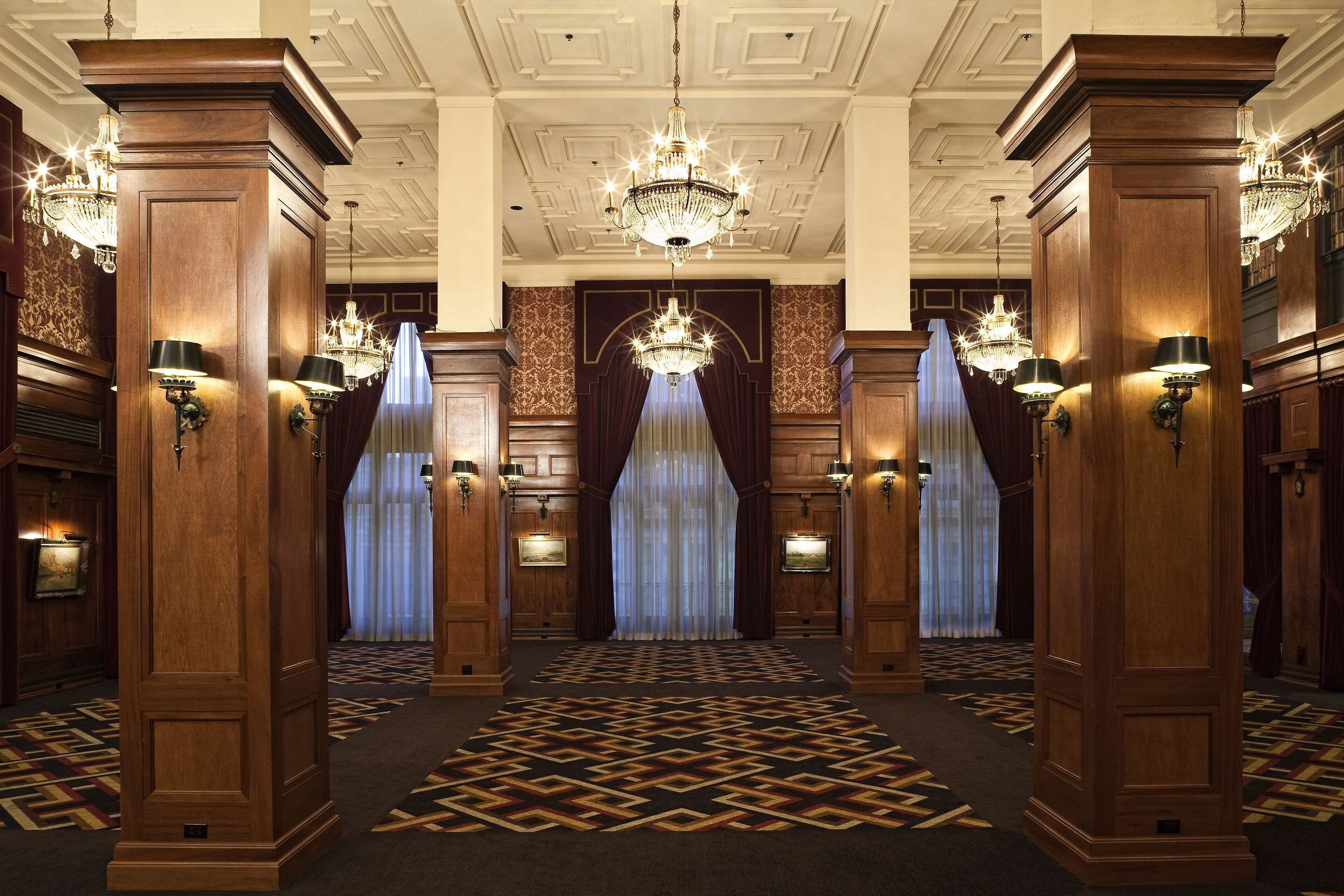 Um hall imponente com painéis de madeira ornamentados, lustres e carpete estampado.