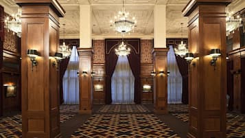 Um hall imponente com painéis de madeira ornamentados, lustres e carpete estampado.