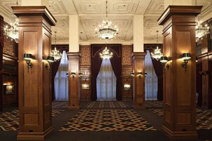 Um hall imponente com painéis de madeira ornamentados, lustres e carpete estampado.