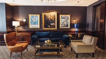 A room with a dark wood-paneled wall, a blue sofa, a patterned floor, a wooden coffee table, and a chandelier.