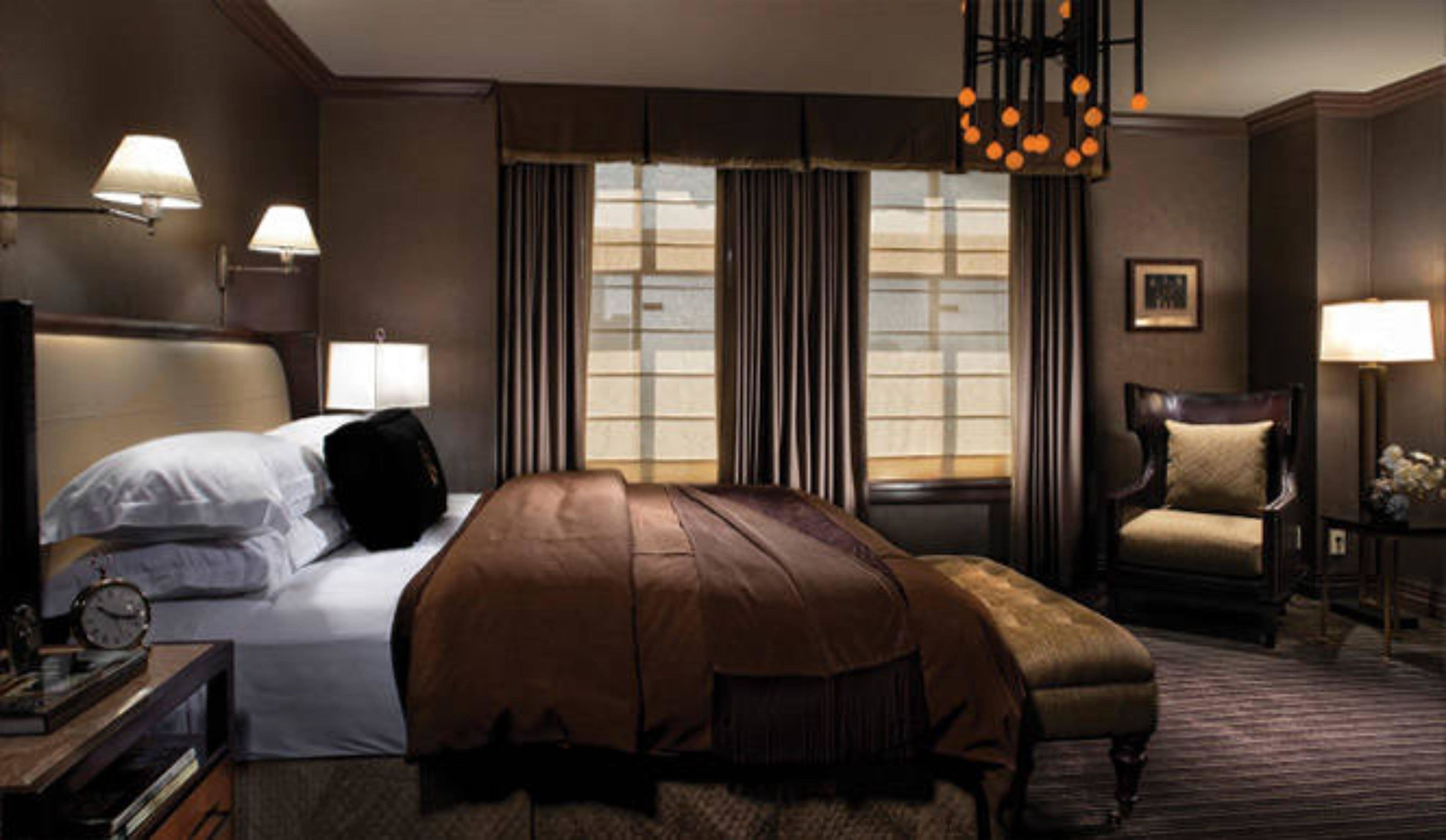 A hotel room with a large bed, a chair, a desk with a lamp, and a window with curtains.