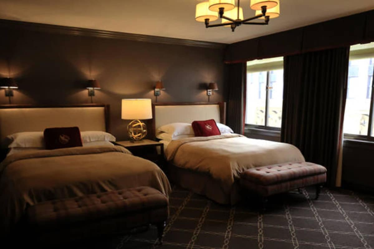 Une chambre d’hôtel avec deux lits, une table de chevet, une lampe et une fenêtre avec des rideaux.