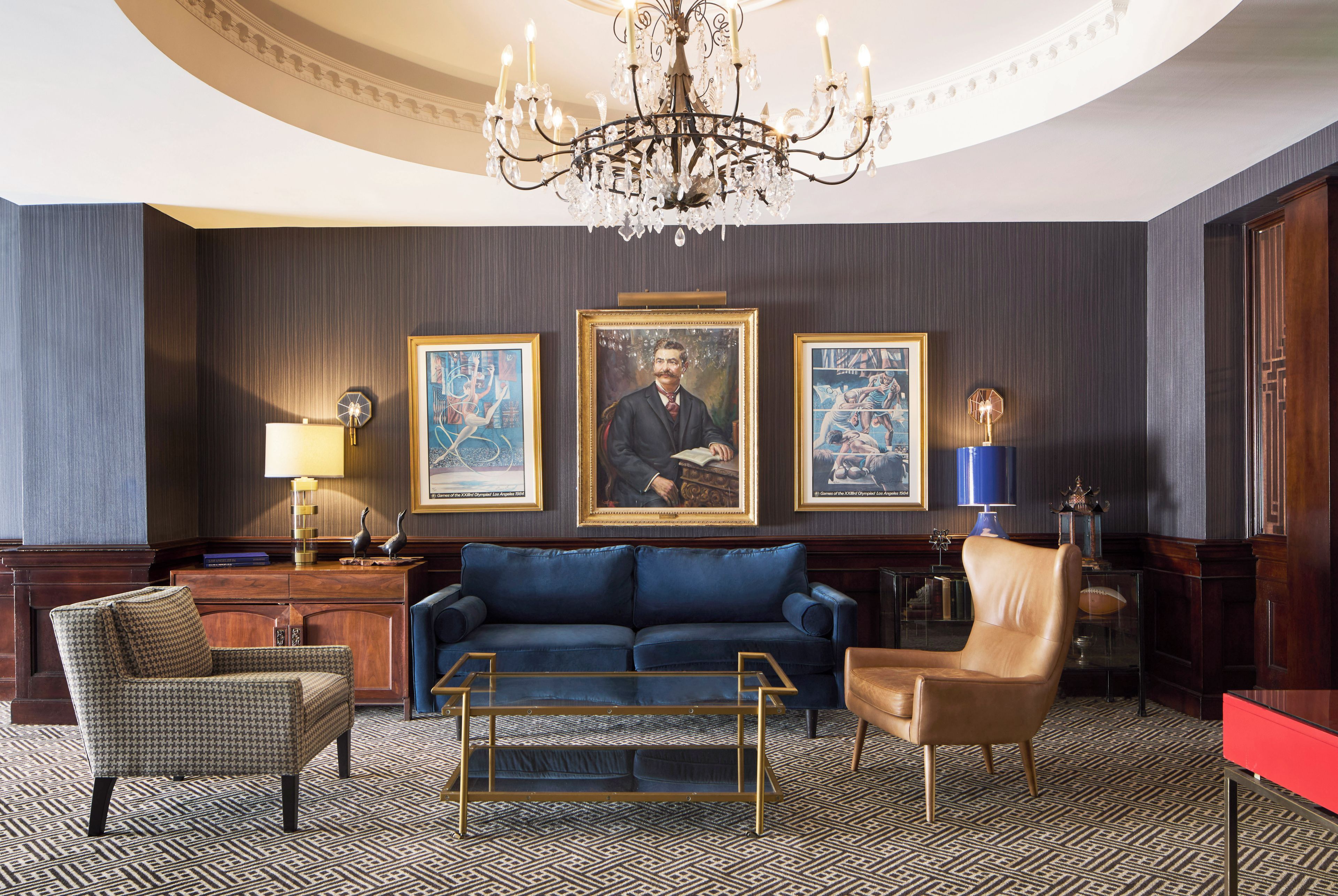 A formal living room with a blue sofa, a chandelier, and three framed artworks on the wall.