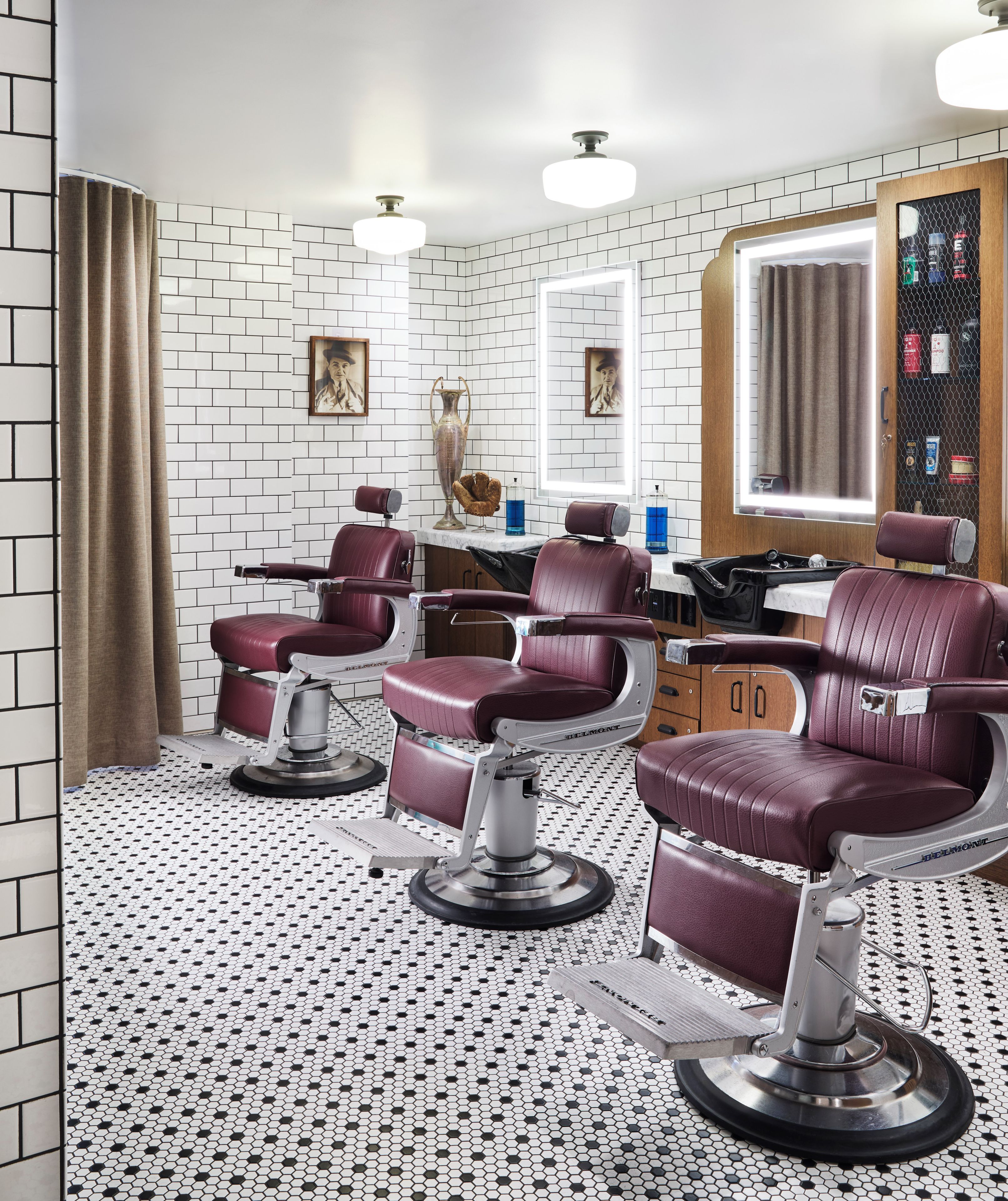 A salon with three barber chairs, a mirror, and a tiled floor.