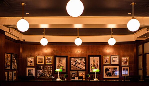 A lobby with wooden paneling, a reception desk, framed pictures on the wall, and hanging spherical light fixtures.