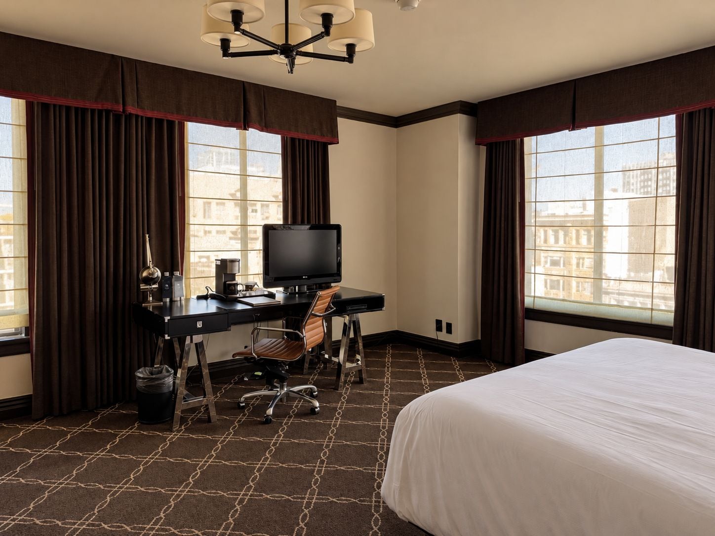Een hotelkamer met een bed, een bureau met een computer, een stoel en een raam met gordijnen.