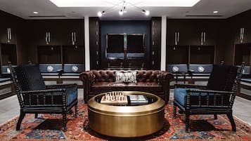 Uma área de estar moderna com uma mesa de centro redonda, duas poltronas estofadas, um sofá de couro e um tapete estampado.