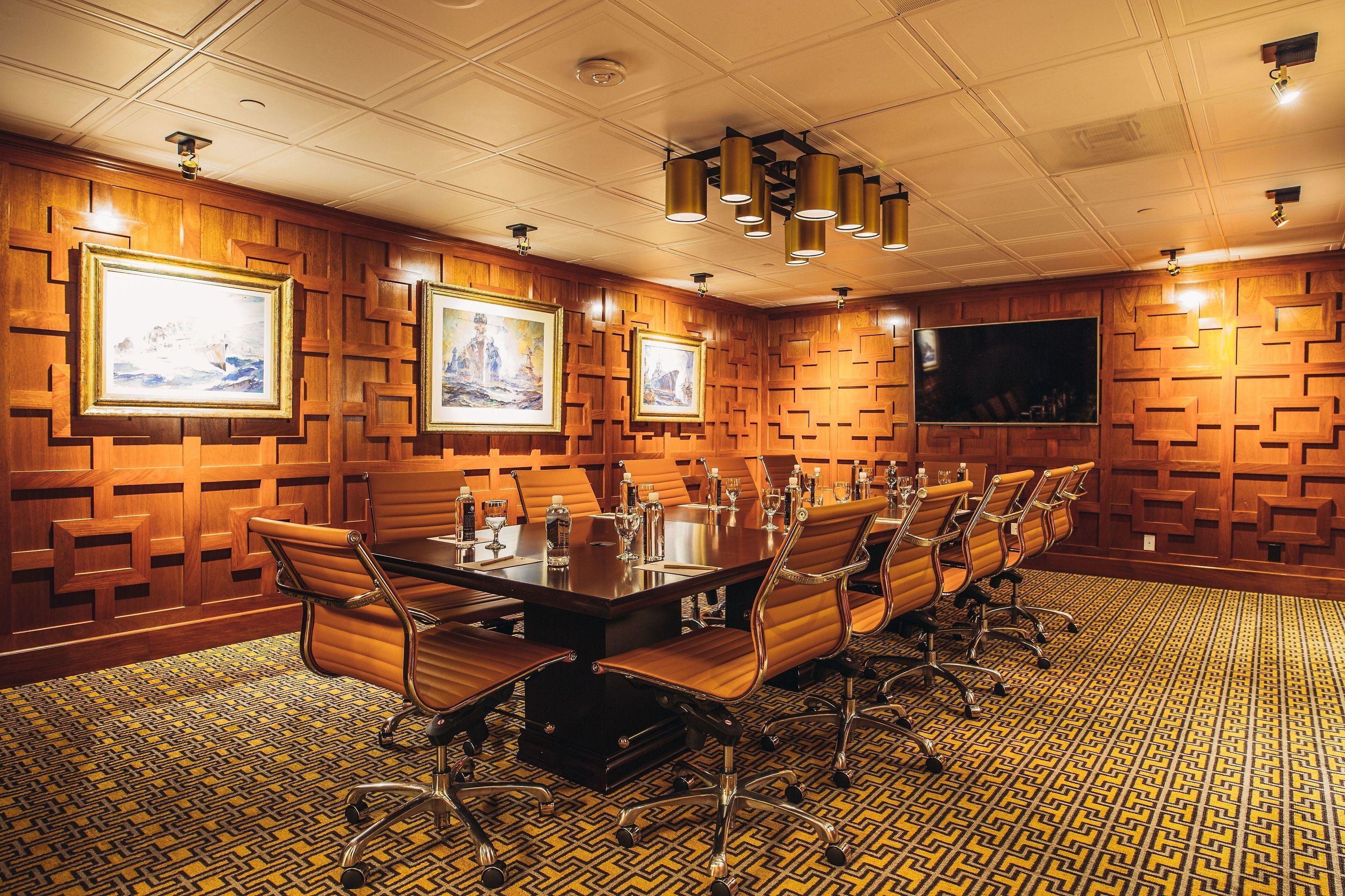 A conference room with a long table, chairs, framed artwork, and a large screen.