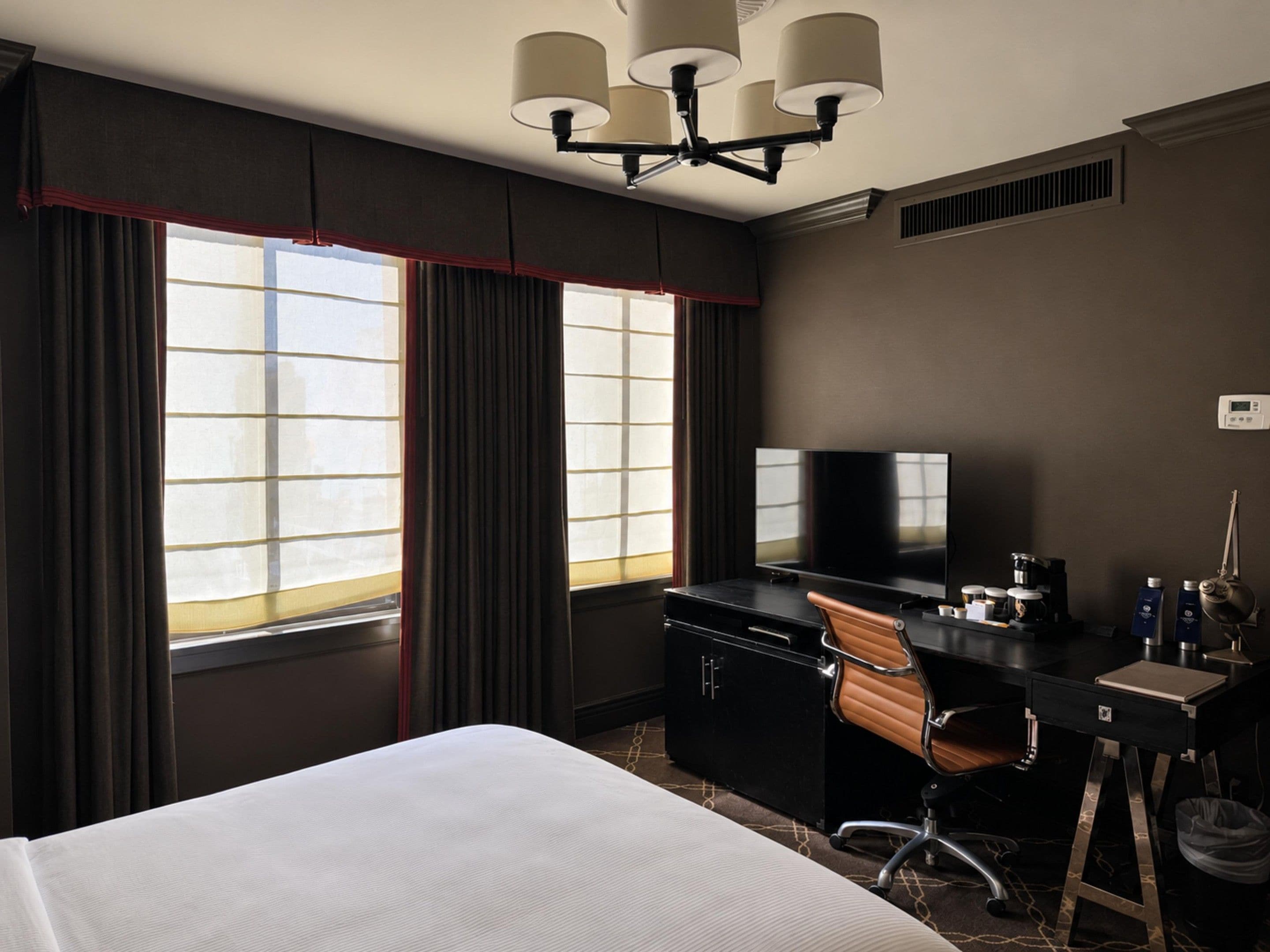 Une chambre d’hôtel équipée d’un lit, d’un bureau, d’une chaise, d’une télévision et d’une grande fenêtre avec des rideaux.