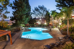 A swimming pool with lounge chairs and umbrellas, surrounded by trees and buildings.