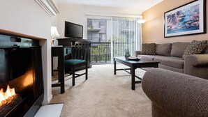 Een woonkamer met een open haard, een bank, een televisie en een balkon met uitzicht op de stad.