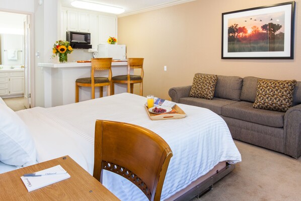 A hotel room with a bed, a dining area with chairs, a microwave, and a framed picture on the wall.