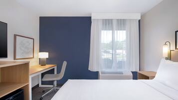 A hotel room with a bed, desk, chair, TV, and window with curtains.