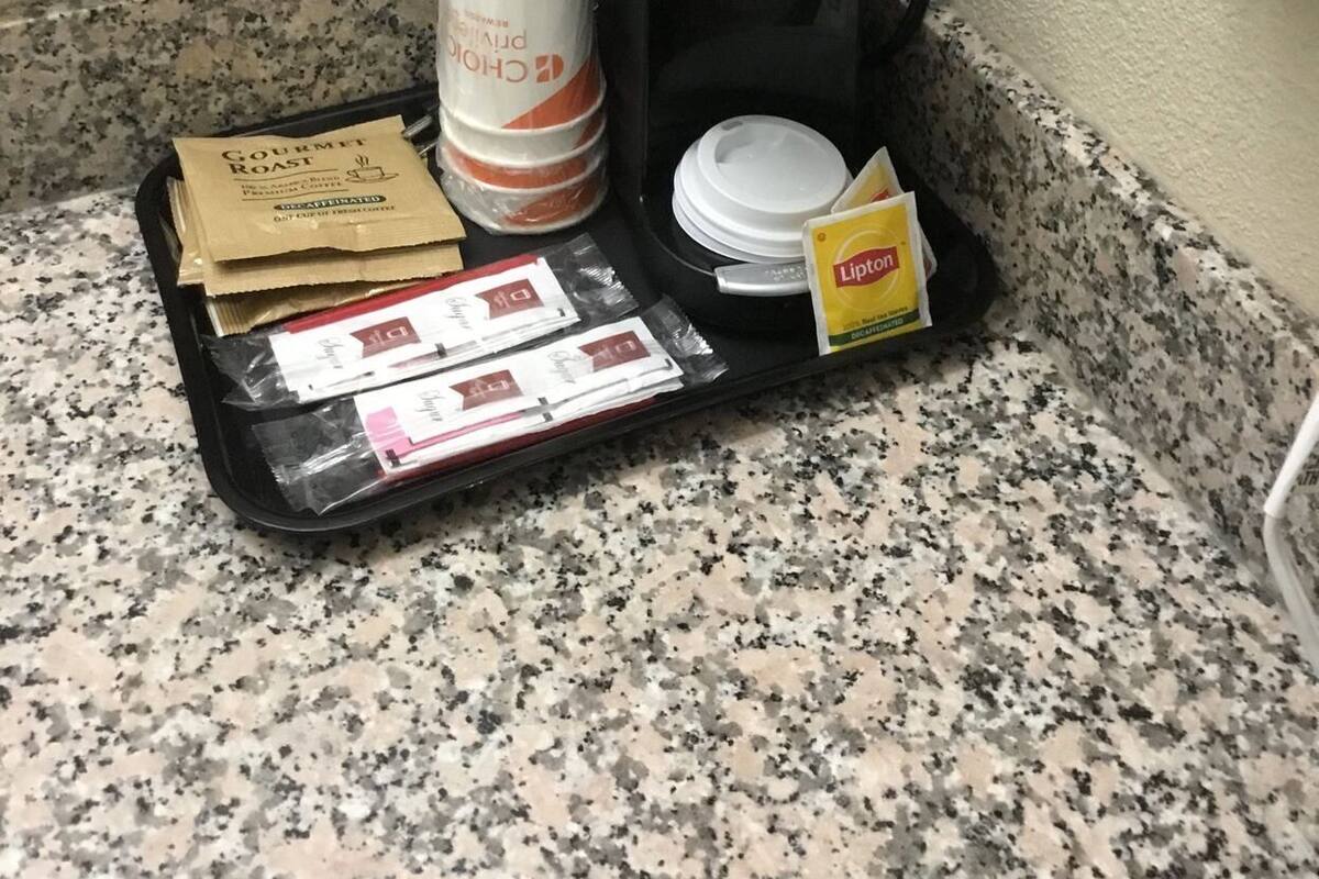 Ett hotellrum har en minibar med en kaffebryggare, en kopp kaffe, ett paket Lipton-te och ett bricka med diverse tillbehör, inklusive en påse med exklusivt, rostade kaffebönor och en burk grädde.
